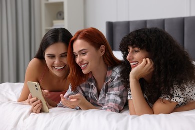 Happy young friends using smartphone on bed at home
