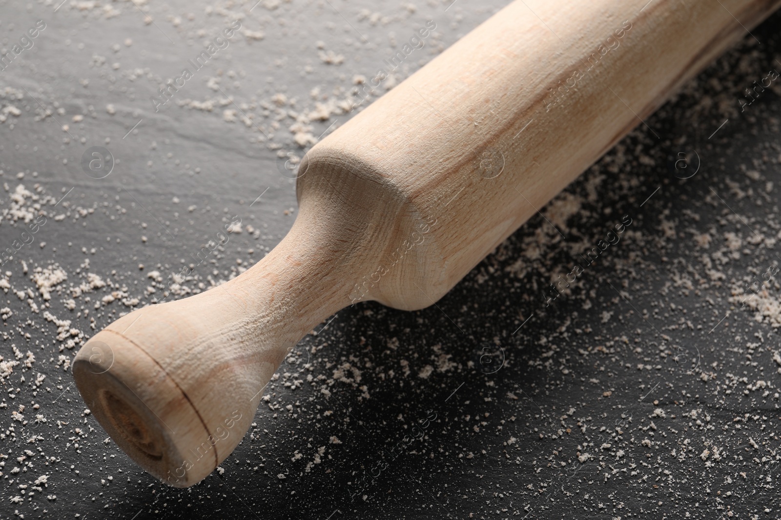 Photo of Scattered flour and rolling pin on dark textured table, closeup