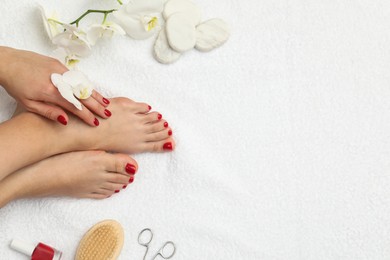 Photo of Woman with stylish red toenails after pedicure procedure and orchid flowers on white terry towel, top view. Space for text