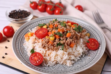 Photo of Tasty dish with fried minced meat, rice, carrot, tomatoes and corn on white wooden table, closeup