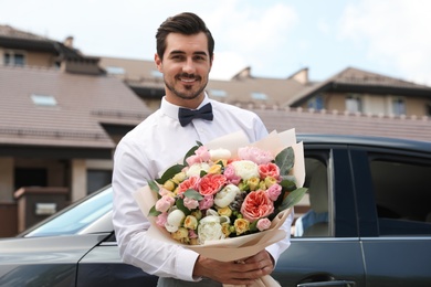 Young handsome man with beautiful flower bouquet near car outdoors