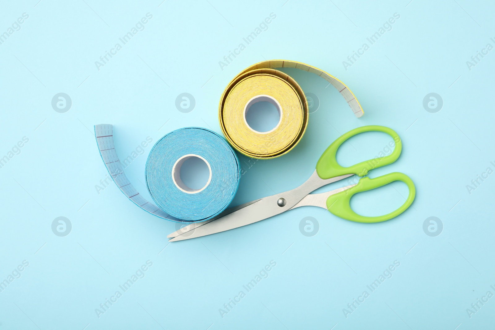 Photo of Bright kinesio tape rolls and scissors on light blue background, flat lay