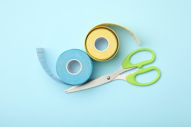 Photo of Bright kinesio tape rolls and scissors on light blue background, flat lay