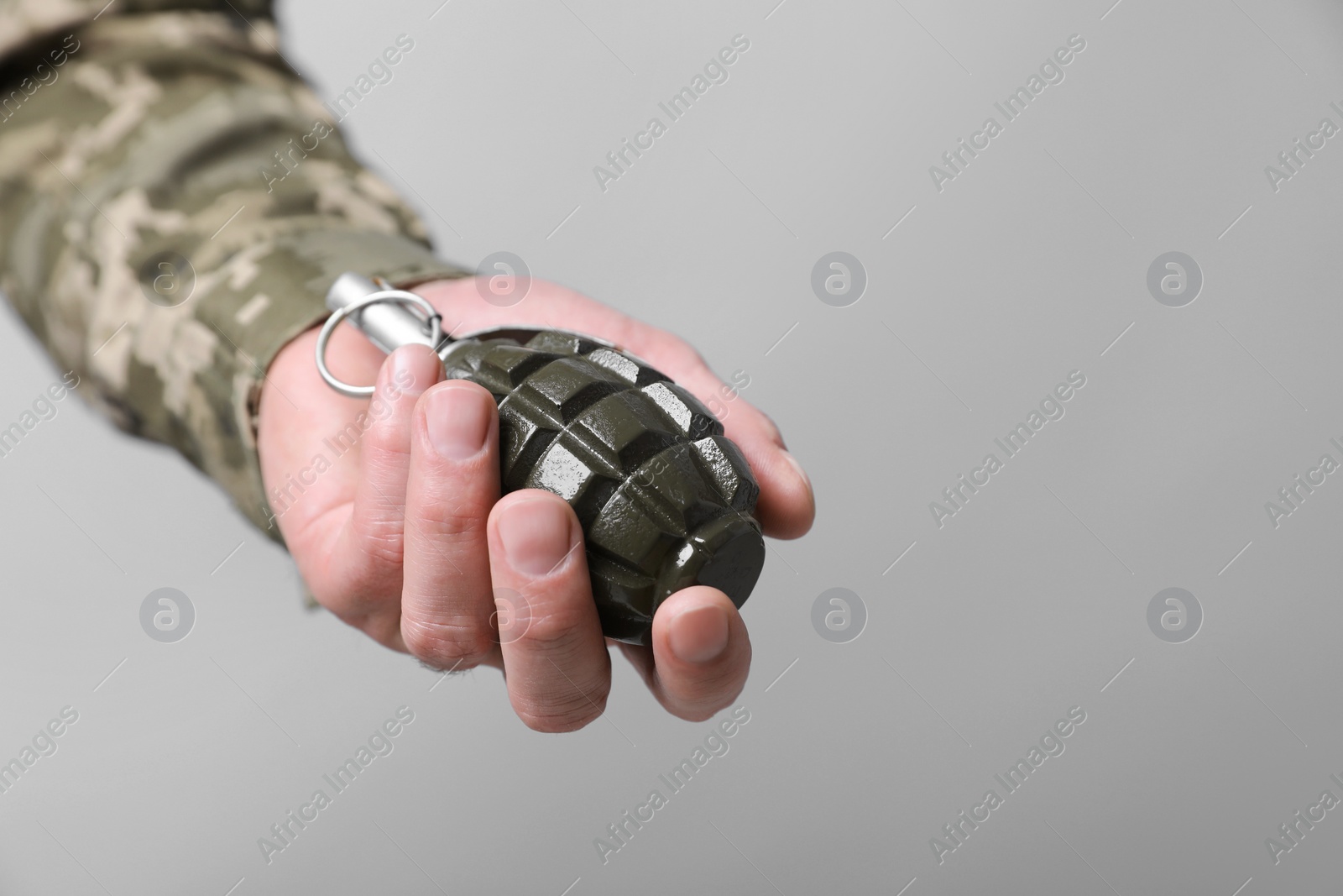 Photo of Soldier holding hand grenade on light grey background, closeup with space for text. Military service