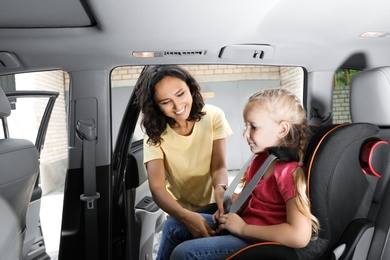 Mother fastening her daughter with car safety belt in child seat. Family vacation