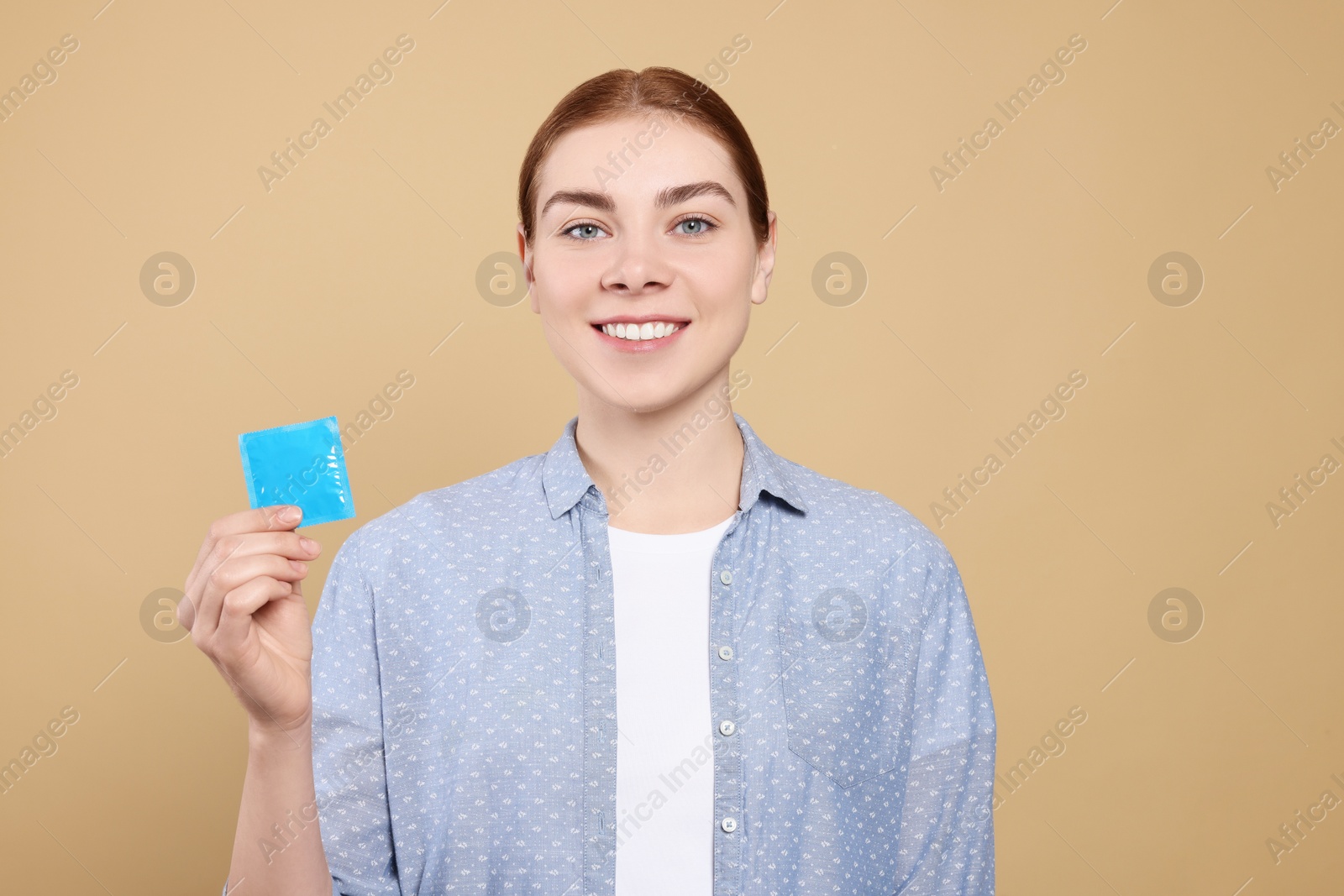 Photo of Woman holding condom on beige background. Safe sex