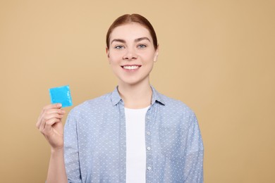 Woman holding condom on beige background. Safe sex
