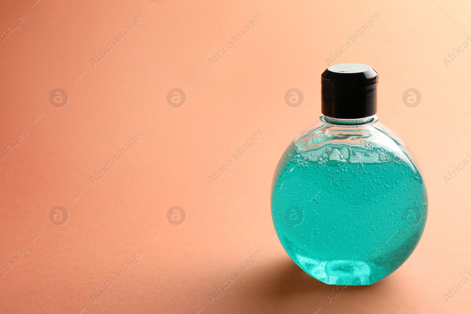 Photo of Bottle of blue cosmetic gel on pale orange background, space for text