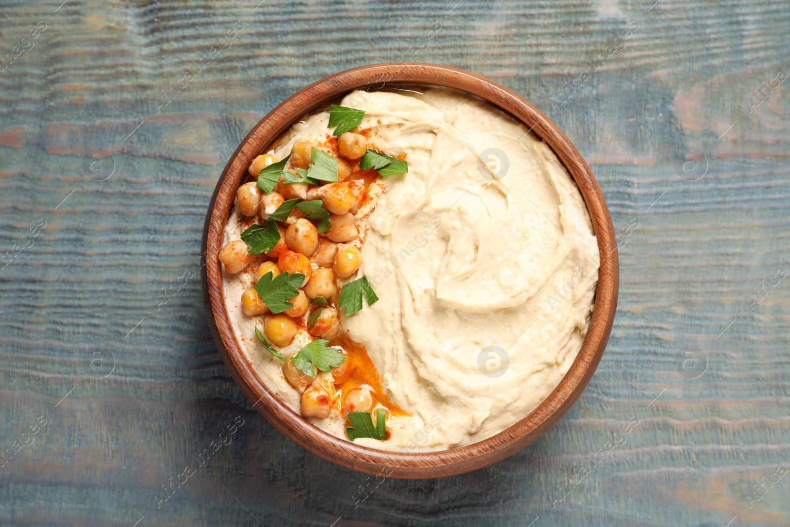 Photo of Bowl of tasty hummus with chickpeas and parsley on wooden table, top view