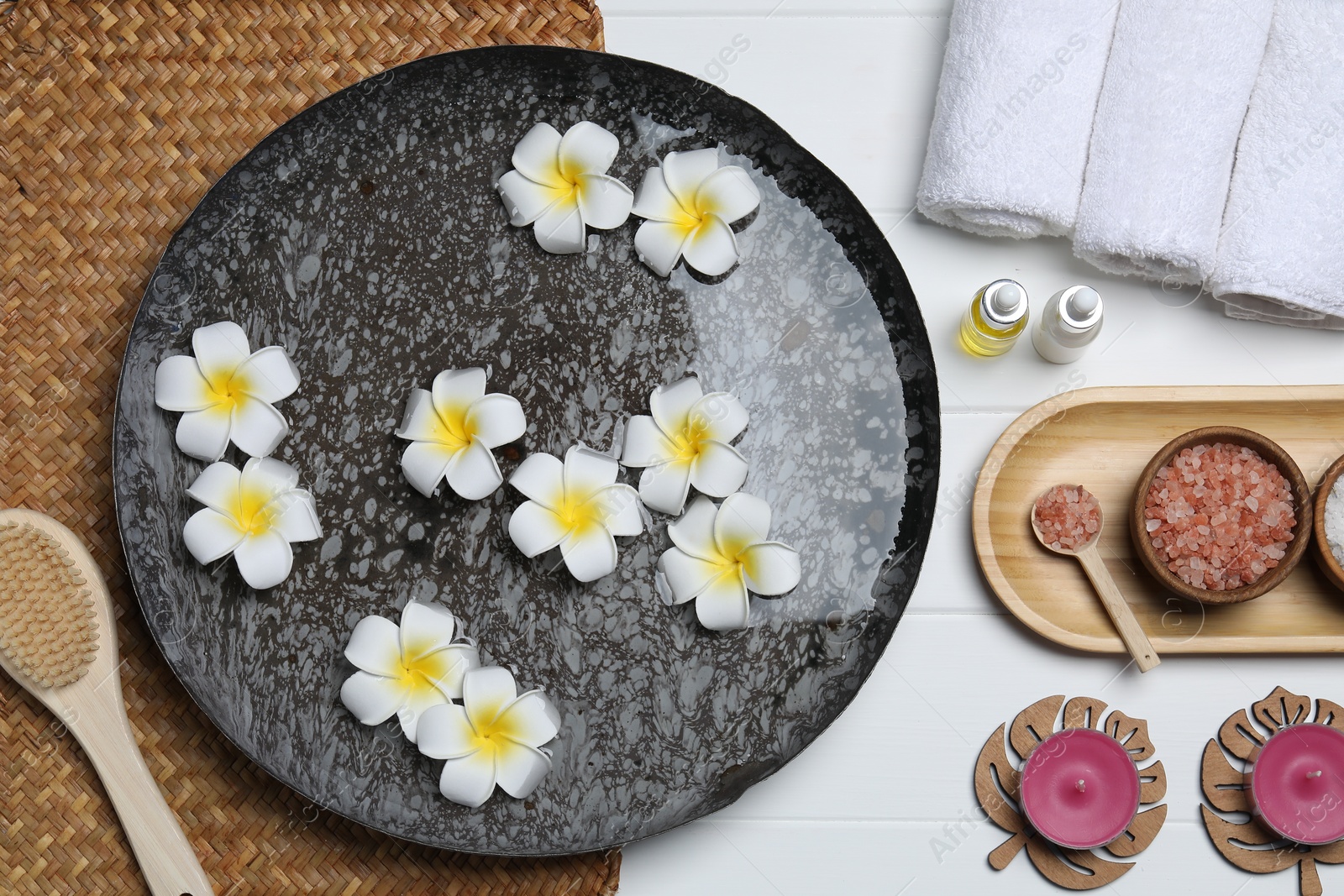 Photo of Bowl of water with flowers and different spa supplies on white wooden table, flat lay