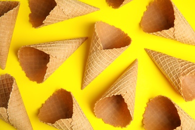 Photo of Empty wafer ice cream cones on yellow background, flat lay