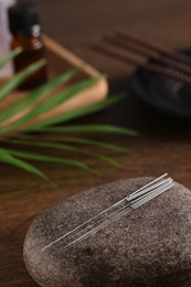 Photo of Acupuncture needles and spa stone on wooden table. Space for text