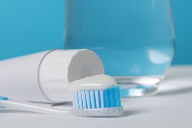Photo of Plastic toothbrush with paste and glass of water on white table against light blue background, closeup