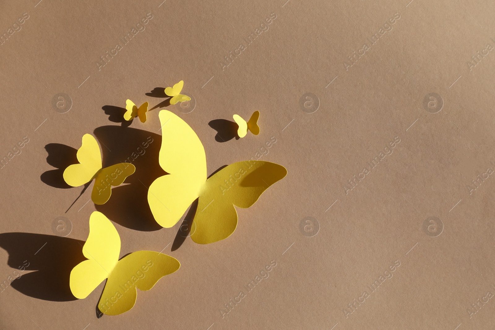 Photo of Yellow paper butterflies on light brown background, top view. Space for text