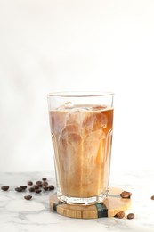 Photo of Refreshing iced coffee with milk in glass and beans on white marble table, space for text