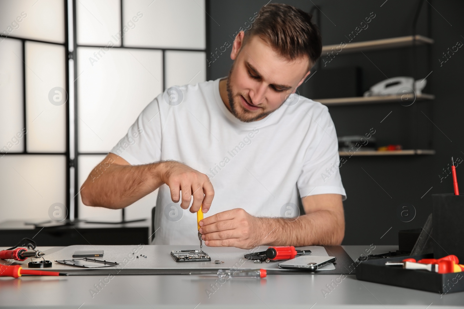 Photo of Technician repairing mobile phone at table in workshop