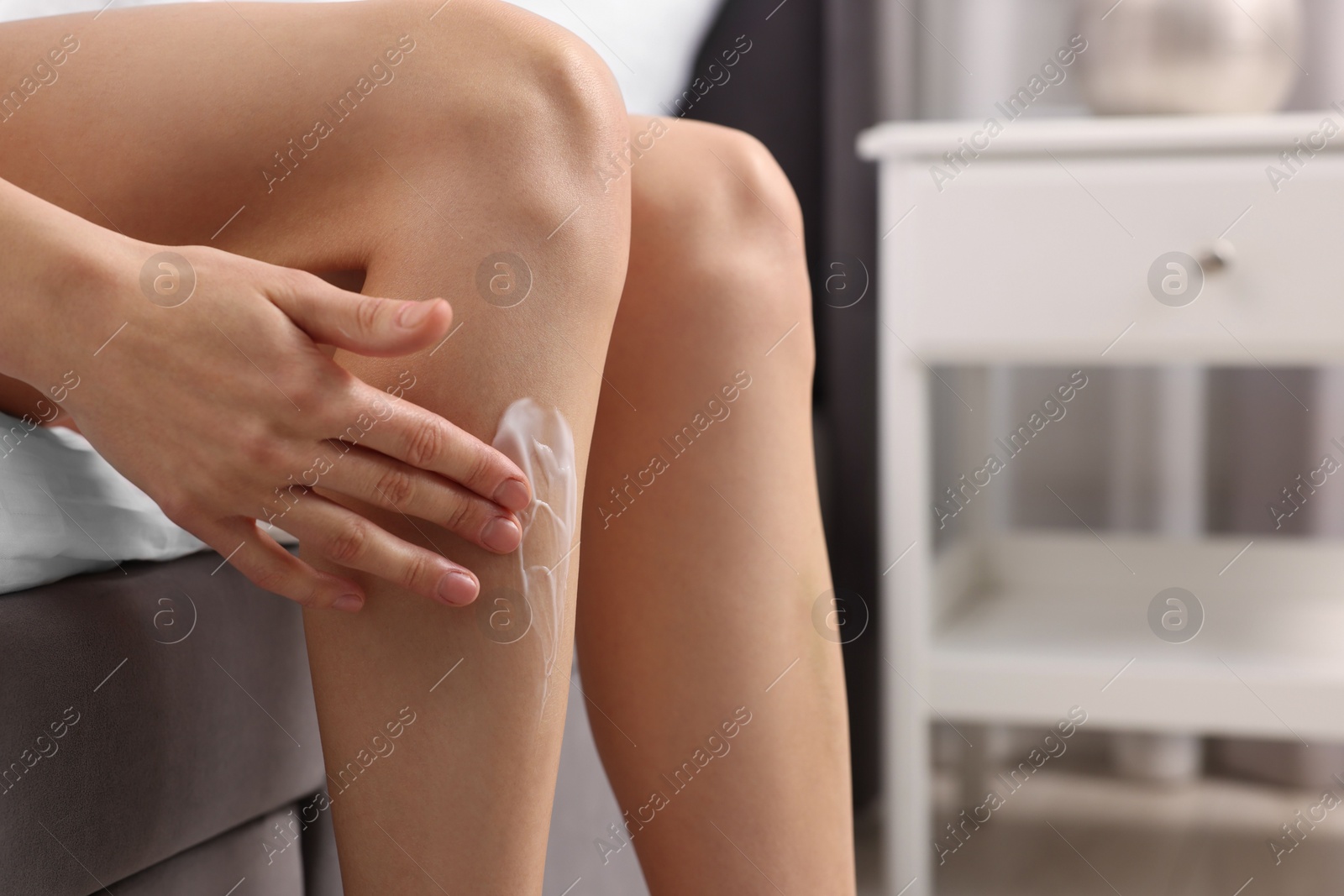 Photo of Woman applying cream onto leg in bedroom, closeup. Space for text