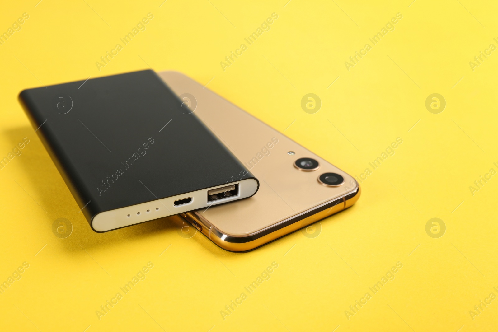 Photo of Mobile phone and portable charger on yellow background