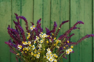 Photo of Beautiful bouquet with field flowers near green wooden wall, closeup