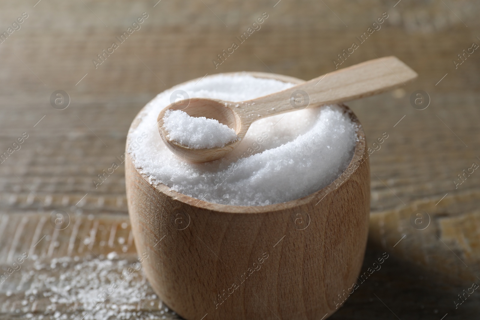 Photo of Organic salt in bowl and spoon on wooden table, closeup