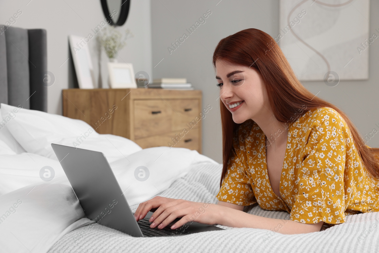 Photo of Happy woman using laptop on bed in bedroom
