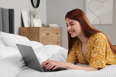 Photo of Happy woman using laptop on bed in bedroom