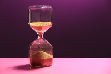 Hourglass with flowing sand on purple background. Space for text