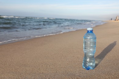 Photo of Plastic bottle of fresh water on wet sand near sea. Space for text