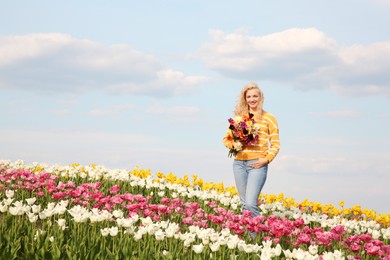 Happy woman with spring bouquet of flowers in beautiful tulip field on sunny day