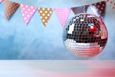 Shiny disco ball hanging over white table. Space for text