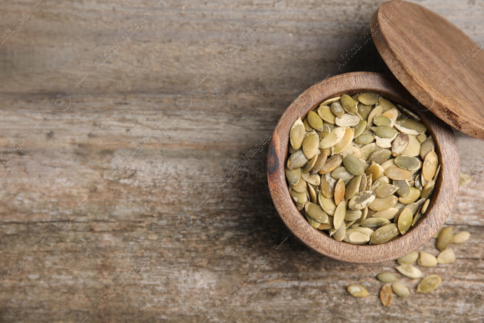 Photo of Dish with pumpkin seeds and lid on wooden table, flat lay. space for text