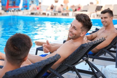 Photo of Happy young friends relaxing on deck chairs near swimming pool