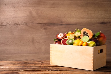 Photo of Different tropical fruits in box on wooden table. Space for text