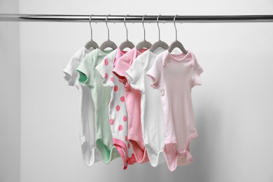 Baby bodysuits hanging on rack near white wall