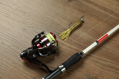 Photo of Fishing rod with spinning reel and bait on wooden background, above view