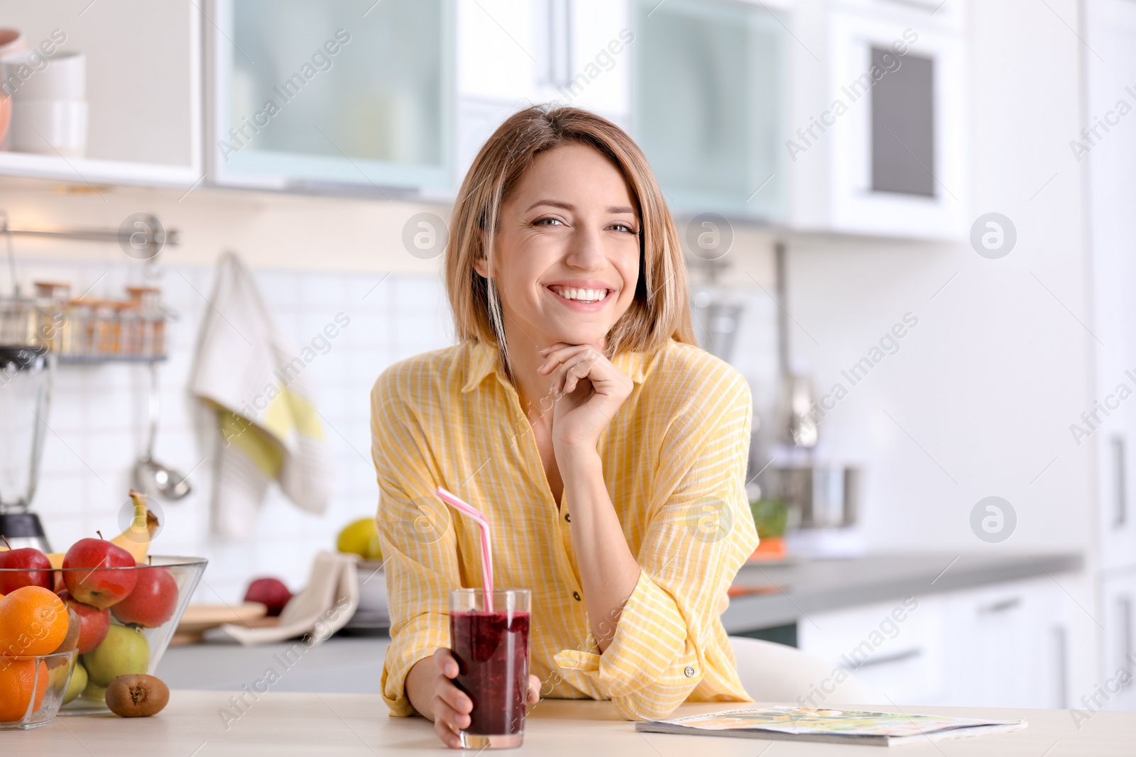 Photo of Young woman with glass of tasty healthy smoothie at table in kitchen