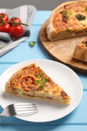 Delicious homemade vegetable quiche and fork on light blue table