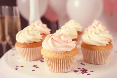 Photo of Stand with cupcakes and blurred balloons on background, closeup