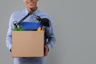 Unemployed young man with box of personal office belongings on grey background, closeup. Space for text
