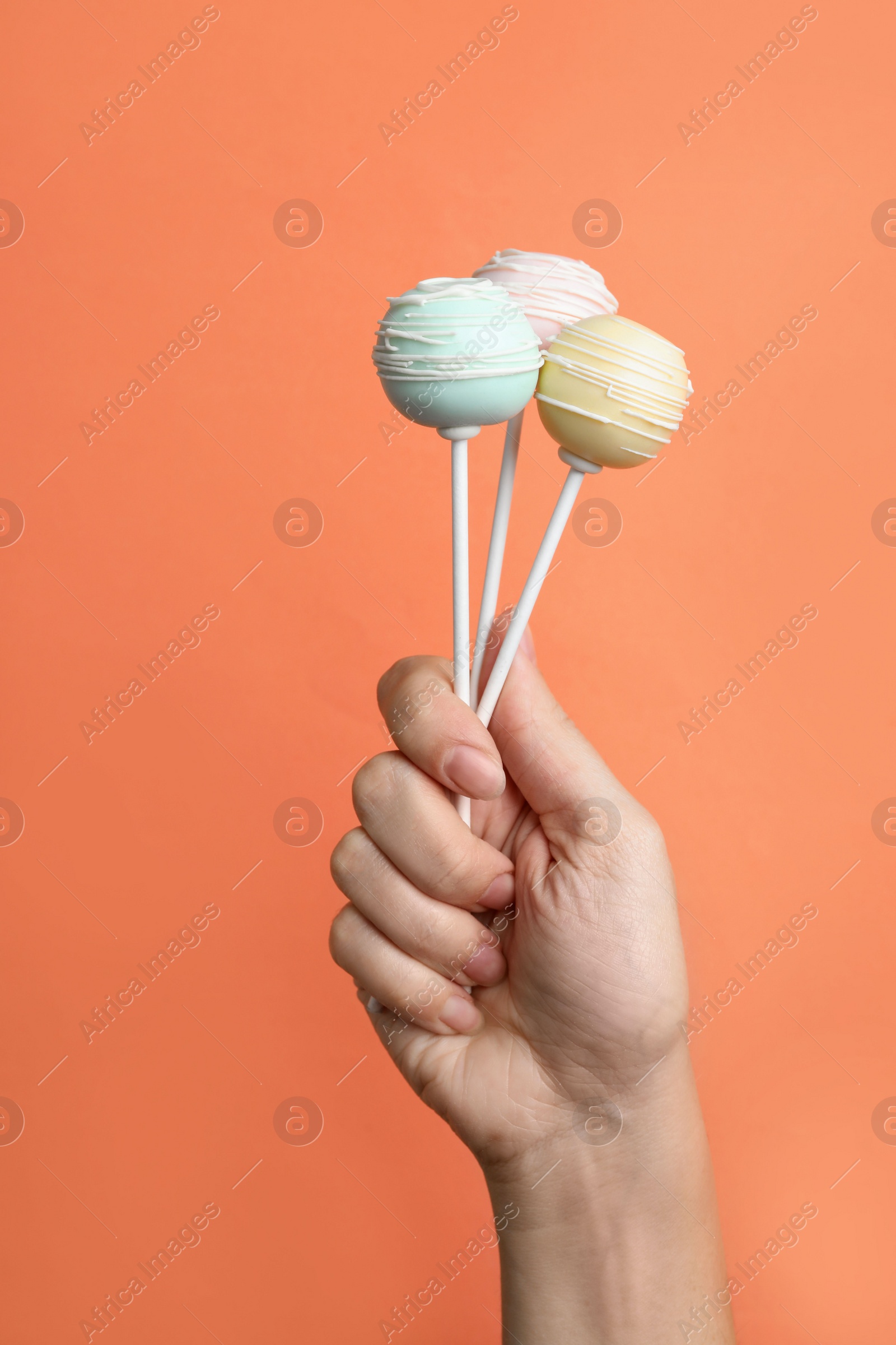 Photo of Woman holding sweet cake pops on coral background, closeup