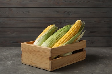 Photo of Corn cobs in crate on grey table