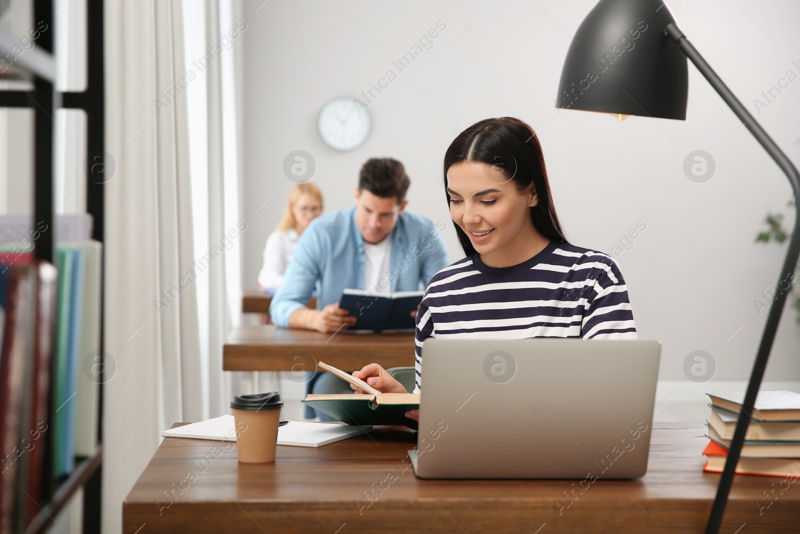 Photo of Young woman reading book at table in library