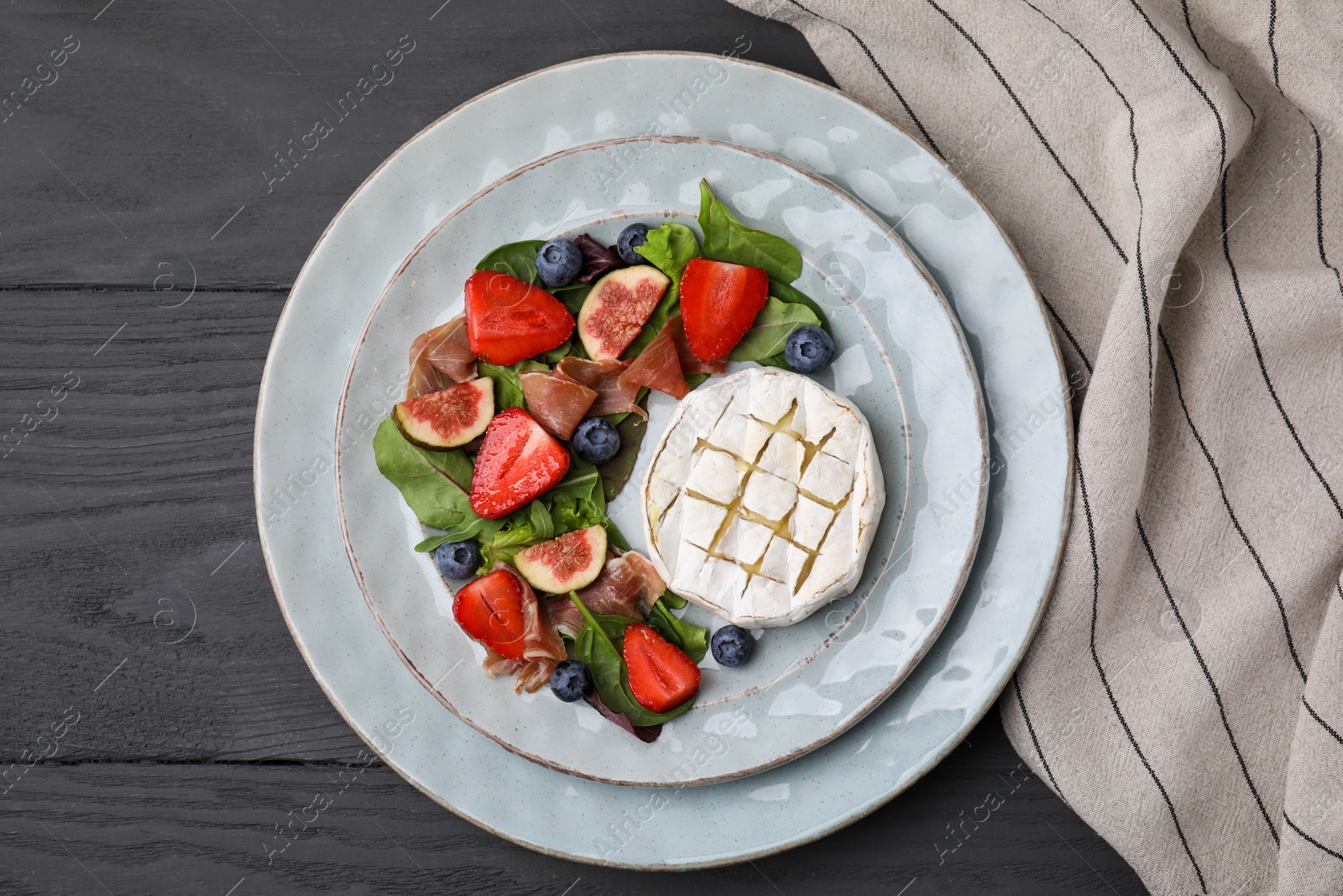 Photo of Delicious salad with brie cheese, prosciutto, figs and strawberries on grey wooden table, top view