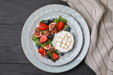 Photo of Delicious salad with brie cheese, prosciutto, figs and strawberries on grey wooden table, top view