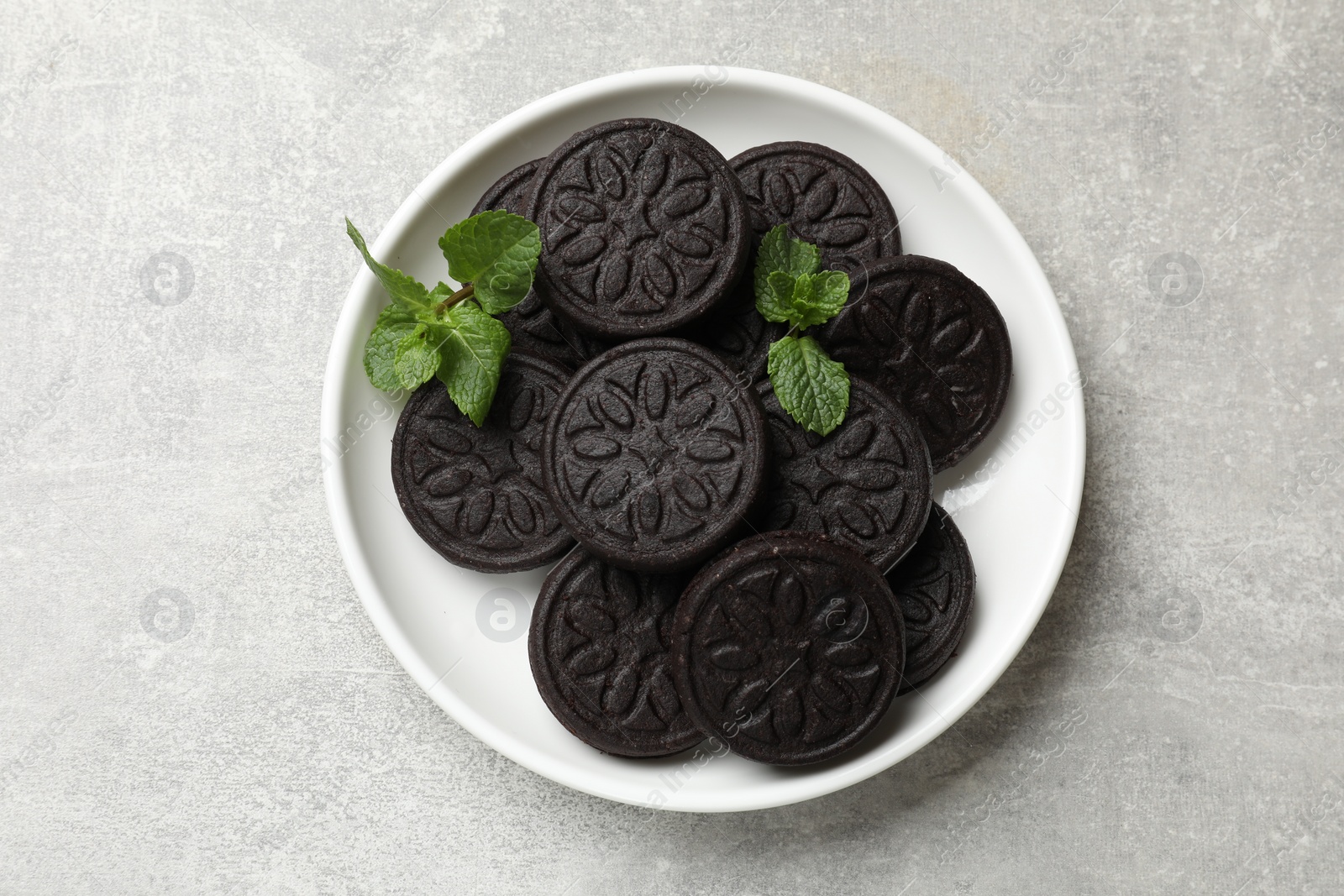 Photo of Plate with tasty sandwich cookies and mint on grey textured table, top view