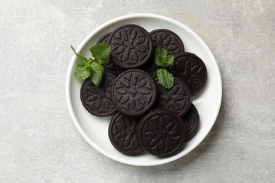 Plate with tasty sandwich cookies and mint on grey textured table, top view