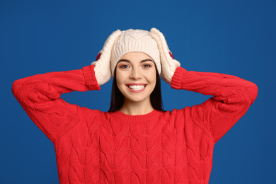 Photo of Young woman wearing warm sweater, mittens and hat on blue background. Winter season
