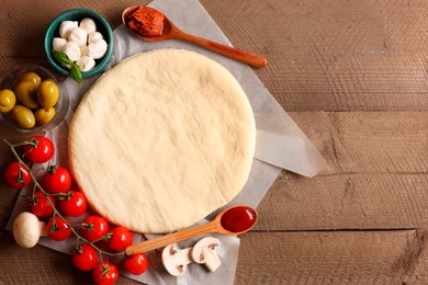 Pizza dough and products on wooden table, flat lay. Space for text