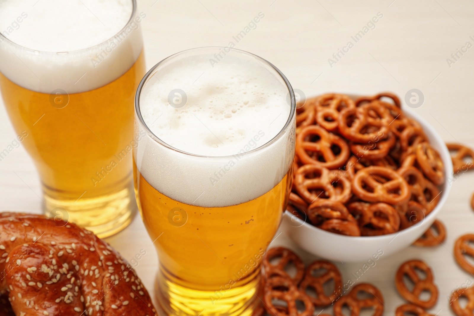 Photo of Tasty pretzels, crackers and glasses of beer on white table, closeup