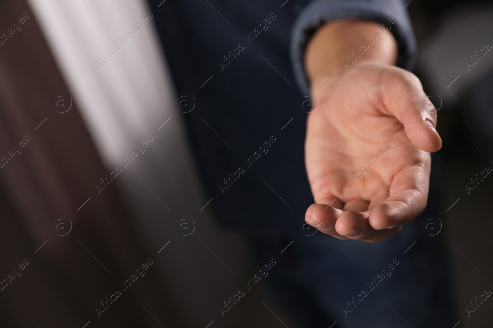 Photo of Man offering helping hand on blurred background, closeup. Space for text